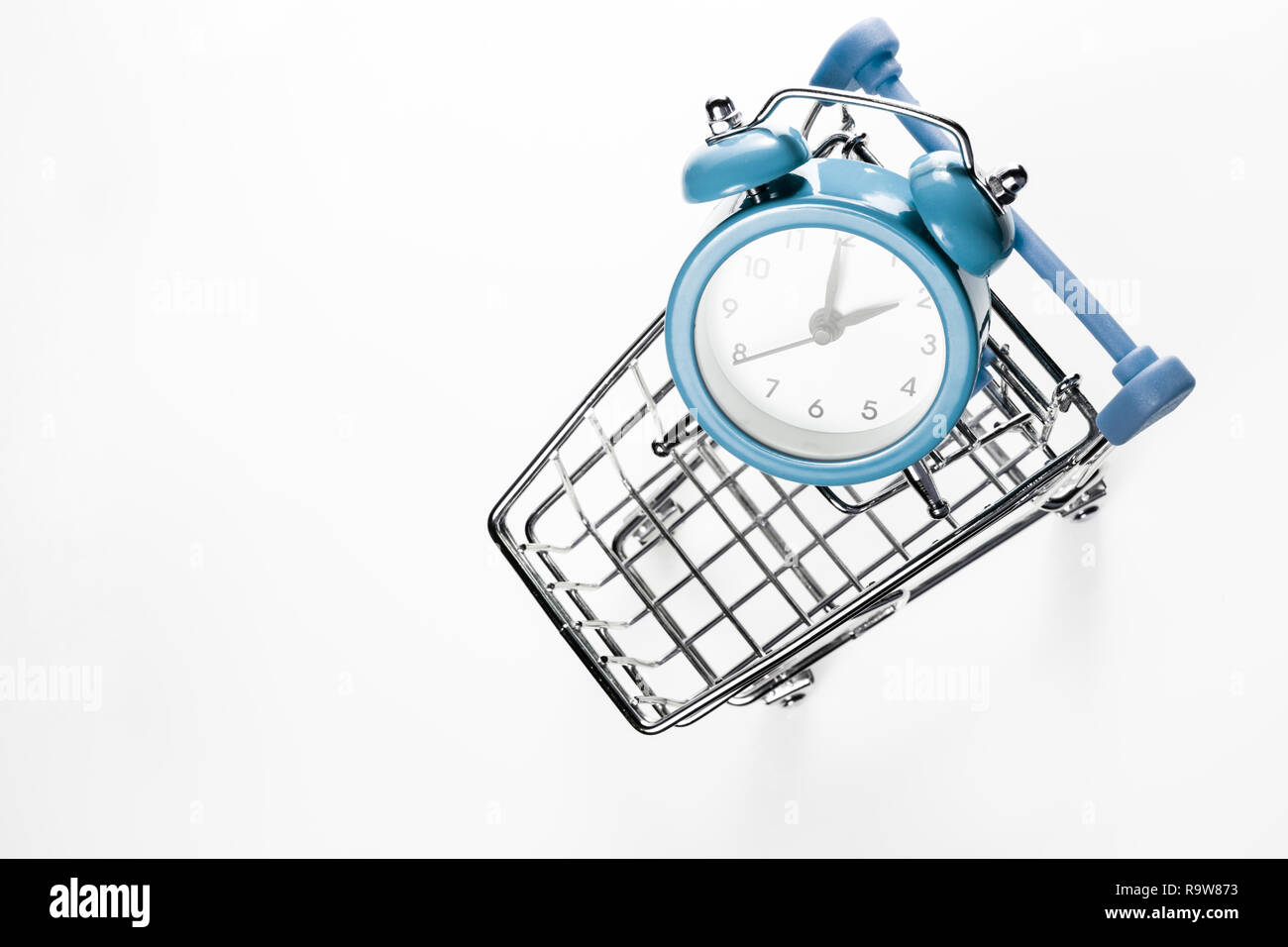 Blue sveglia nel carrello della spesa su uno sfondo bianco. Concetto - tempo di acquistare. Vista da sopra. Foto Stock