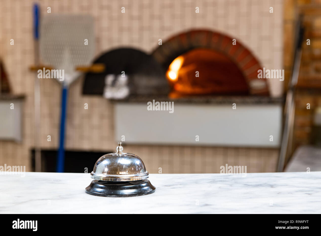 Close up della campana di servizio in pizzeria piano di lavoro, lo sfondo sfocato con forno a legna e Rosso fuoco Foto Stock