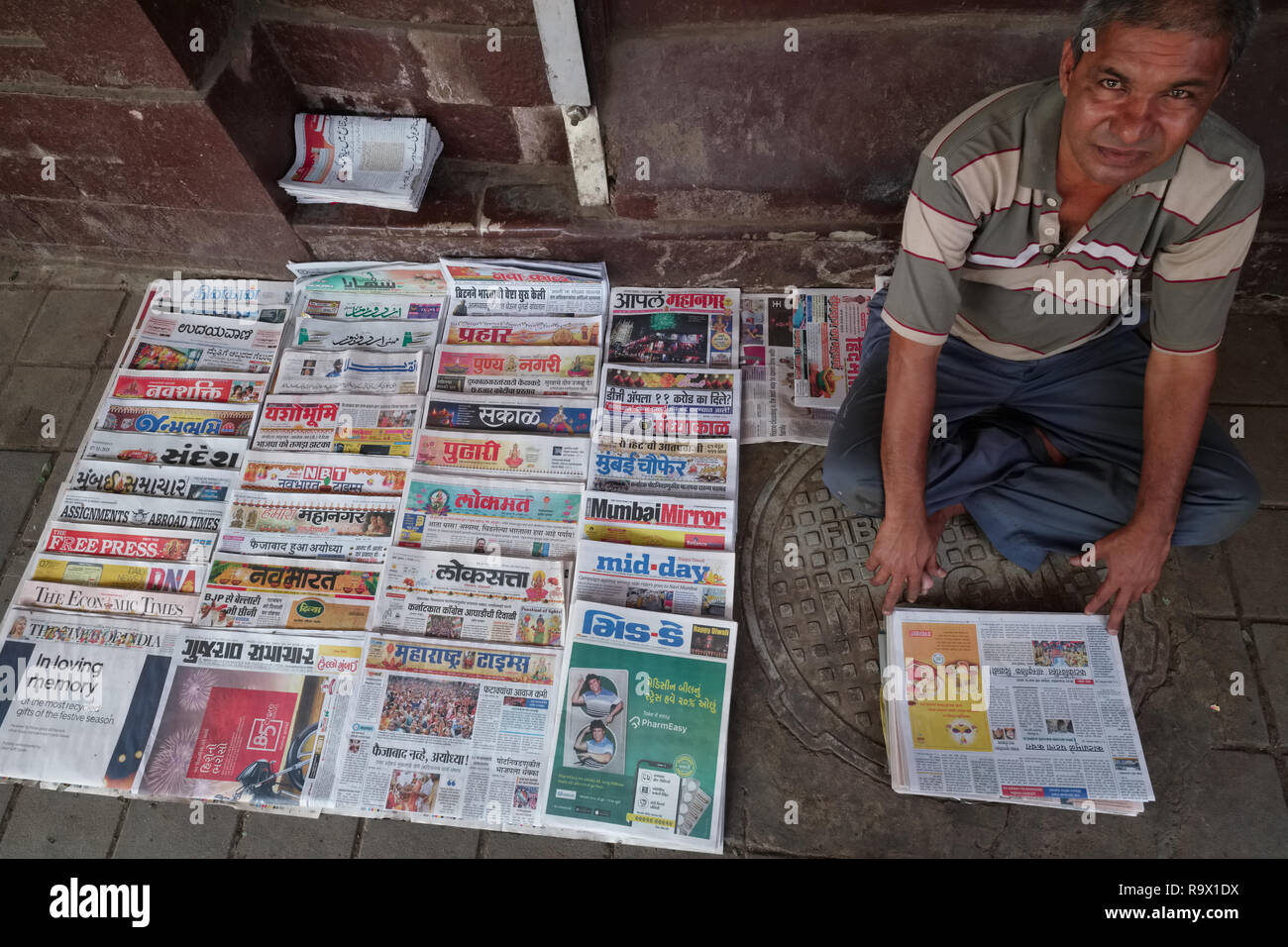 Un giornale fornitore su un sentiero in Mumbai, India, con una varietà di documenti in inglese, hindi e regionali lingue indiane Foto Stock
