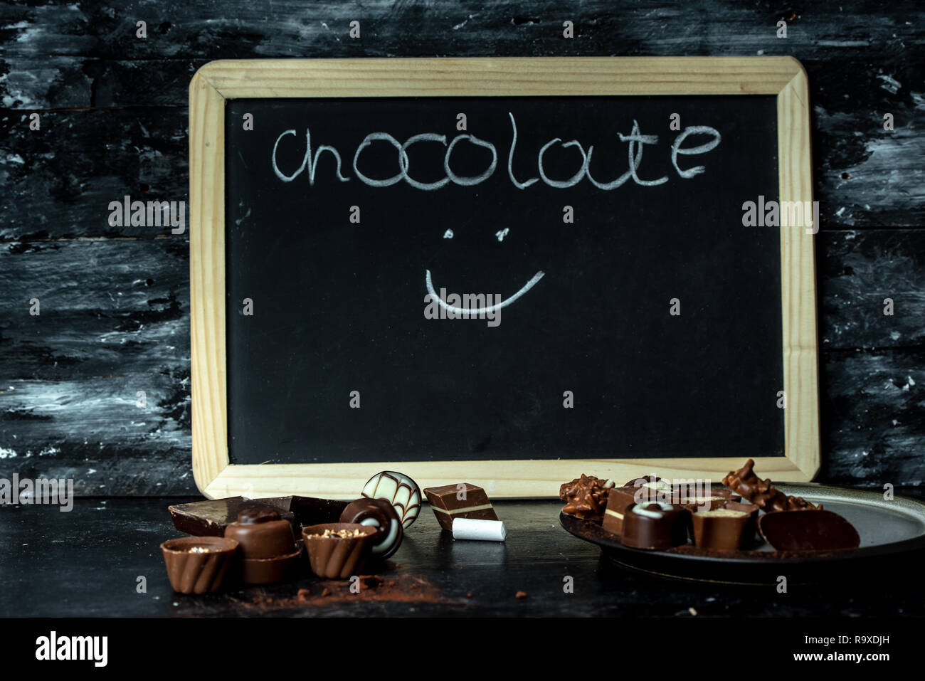 Diversi, dolci praline di cioccolato fondente, al latte e bianco su di un legno scuro sfondo, accanto a Chalk board con la parola cioccolato Foto Stock