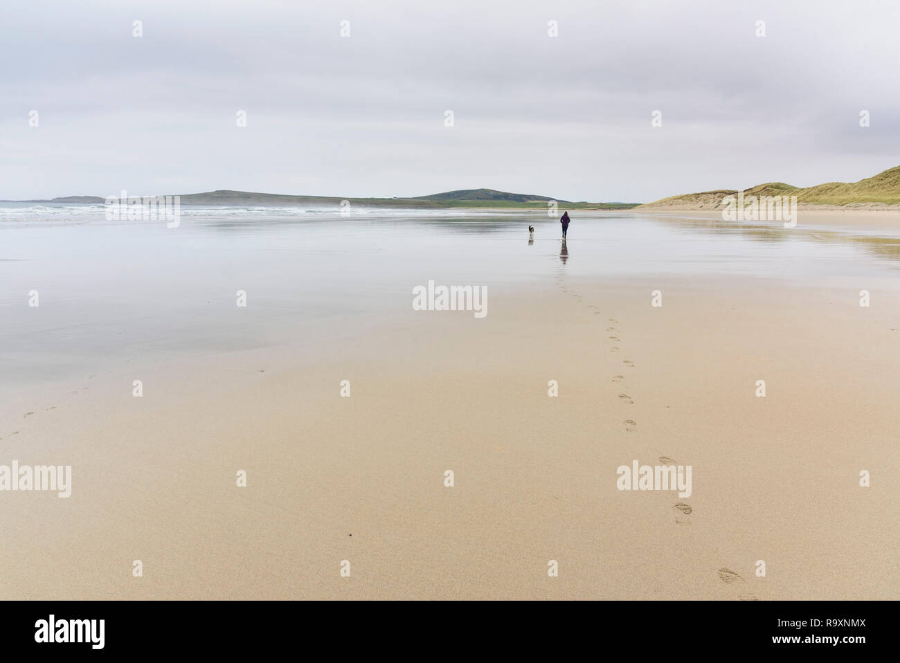 Donna che cammina il suo cane lungo la baia di Machir, Traigh Mhachir beach, Rhinns di Islay, Ebridi Interne, Argyll & Bute, Scozia Foto Stock