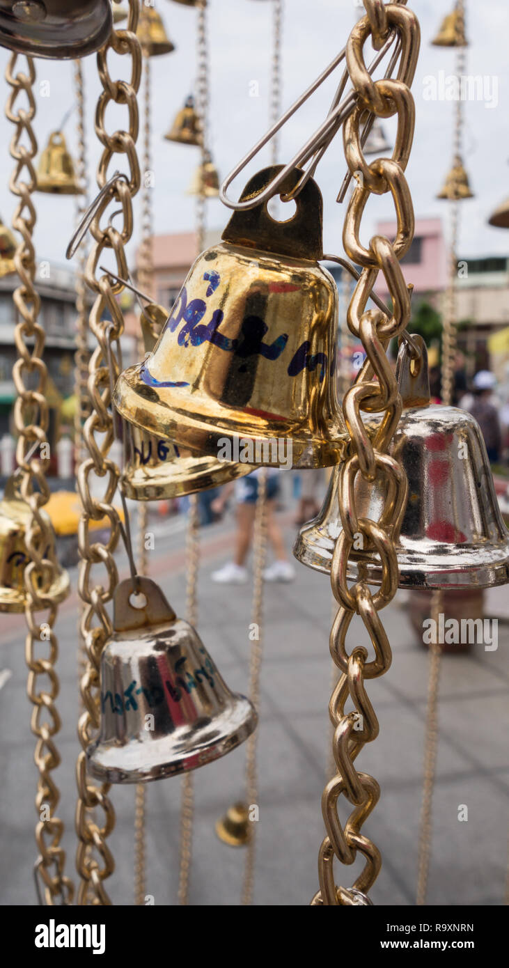 Metallo oro campane, per fortuna nella fede buddista, su una catena al di fuori di un tempio a Bangkok, in Thailandia Foto Stock