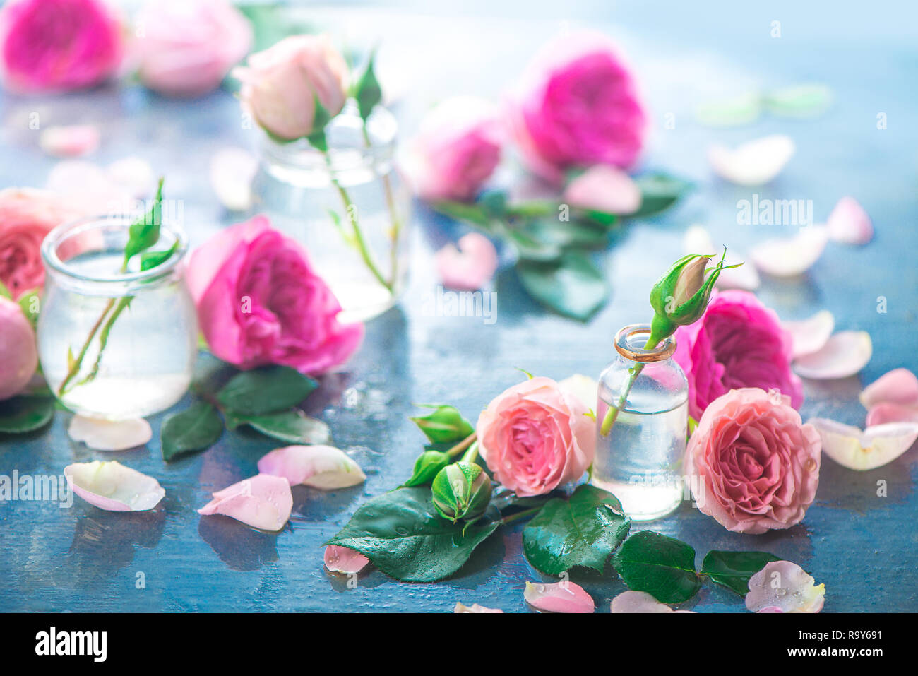 Bottiglie di vetro con rosa peonia rosa su sfondo chiaro con copia spazio. Intestazione femminile con petali e fiori in toni pastello Foto Stock