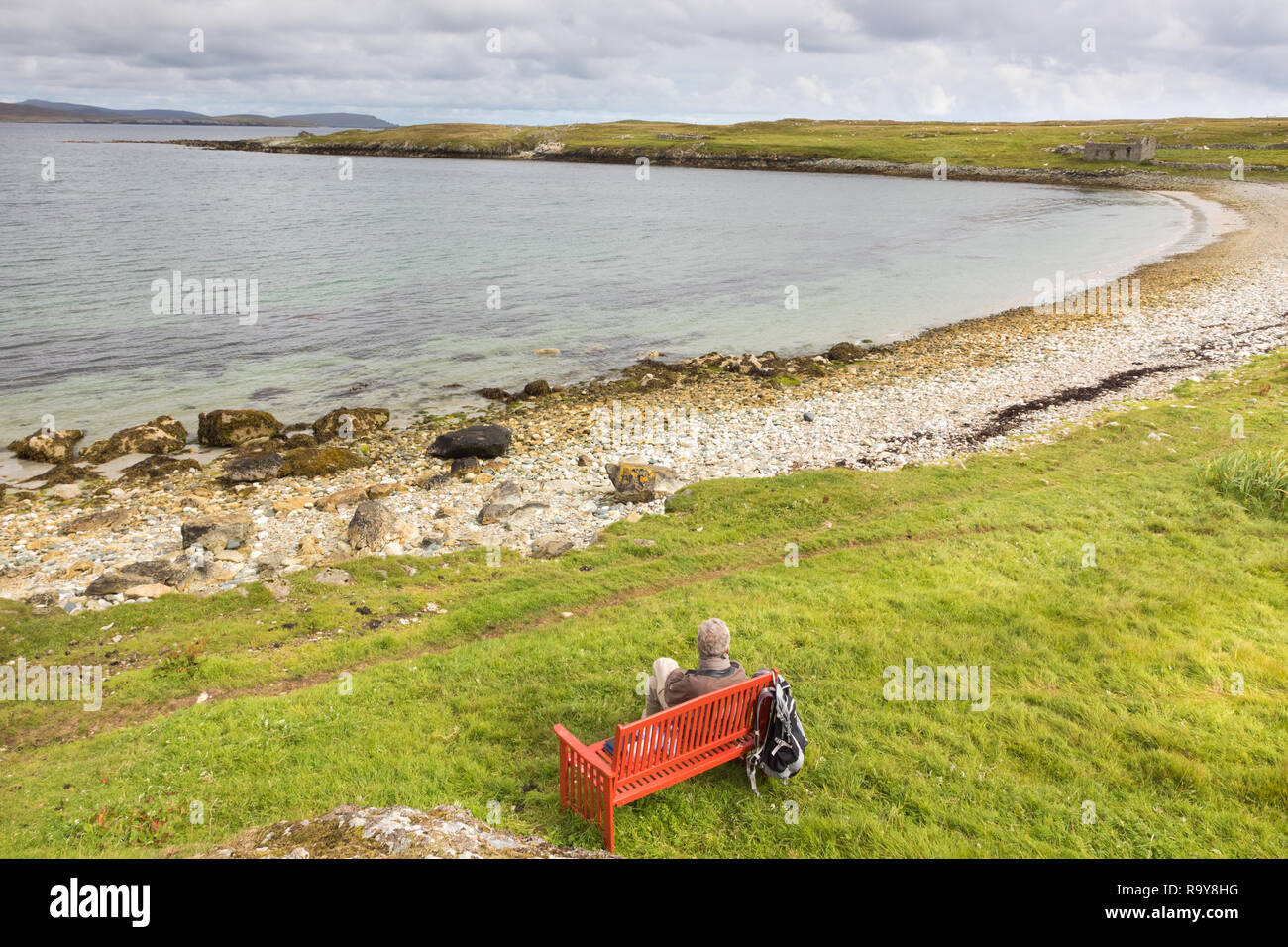 La singola persona seduta su una panchina rossa su una spiaggia sul Unst, Isole Shetland. Foto Stock