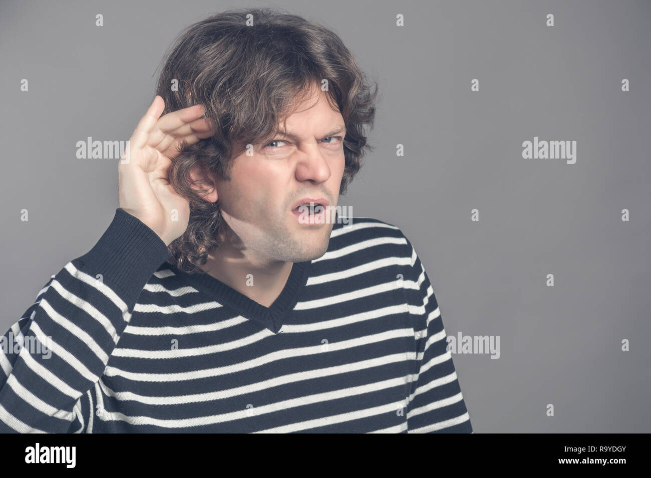 Infelice di udito collocando man mano sull'orecchio chiedere a qualcuno di parlare o ascoltare le cattive notizie, isolata su uno sfondo grigio. Emozione negativa fac Foto Stock