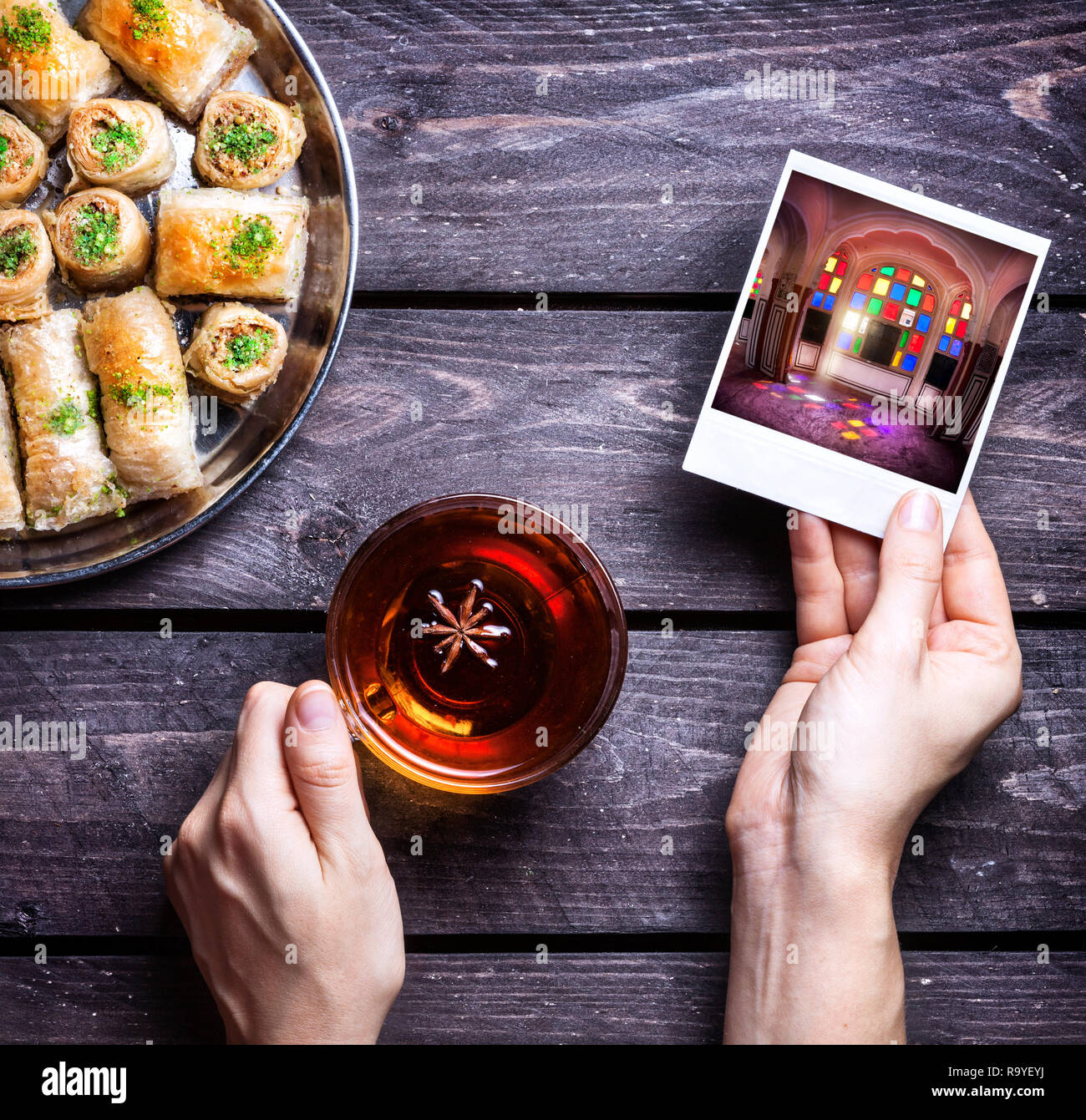 Le mani con la foto del Rajasthan palace e tè badyan vicino al bagno turco baklava su sfondo di legno Foto Stock