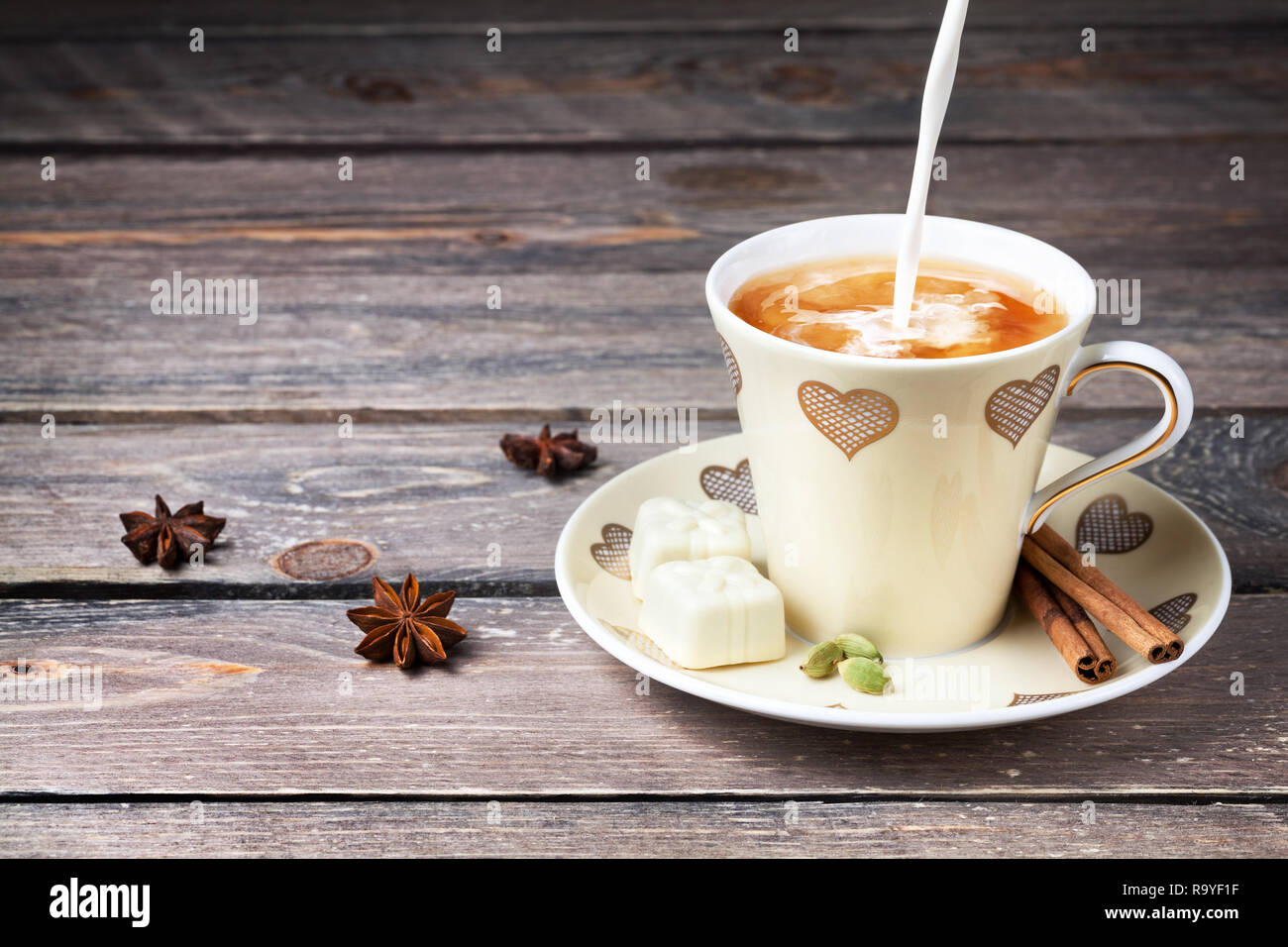 Indian Masala Tè con latte, cannella, anice stellato e spezie cardamomo in tazza con cuori sul tavolo di legno Foto Stock