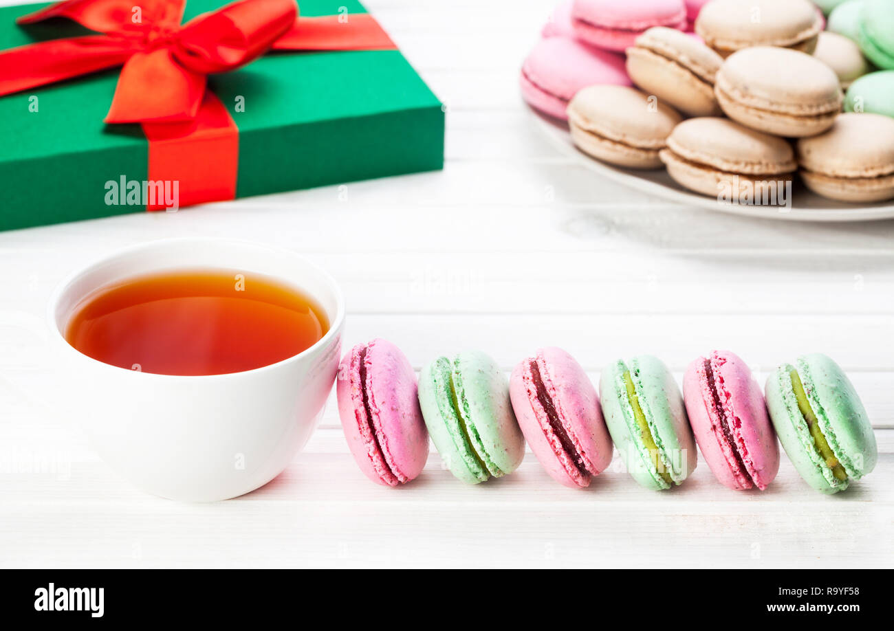 Colorati macarons francese vicino a tazza di tè e la presente casella di Natale su sfondo bianco Foto Stock