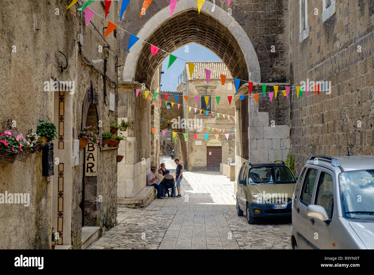 Bandiere colorate appendere al di sopra di una strada di Casertavecchia, Italia. Un gruppo di persone sta parlando sotto l'arco del campanile di questa città medievale. Foto Stock