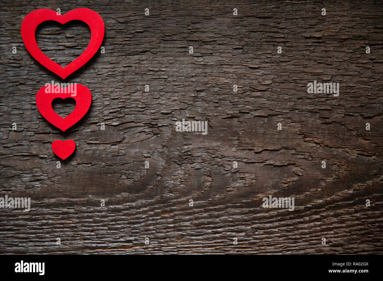 Tre cuori rossi sono situati su un vecchio legno marrone scheda secco, uno meno dell'altro. Il giorno di San Valentino Card Foto Stock