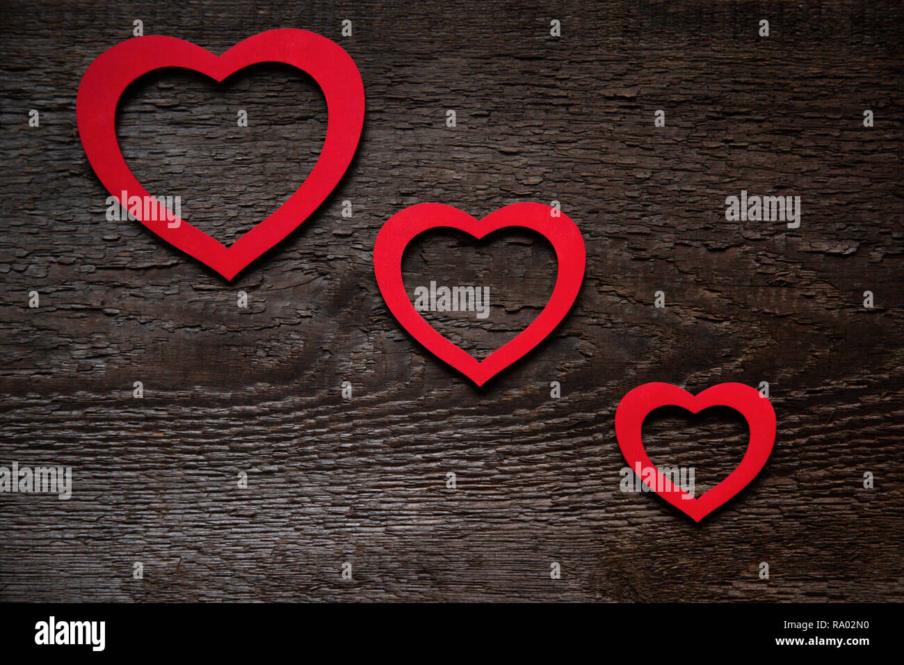 Tre cuori rossi sono disposti in diagonale su un vecchio legno marrone tavola di legno, uno più piccolo dell'altro. Il giorno di San Valentino Card Foto Stock
