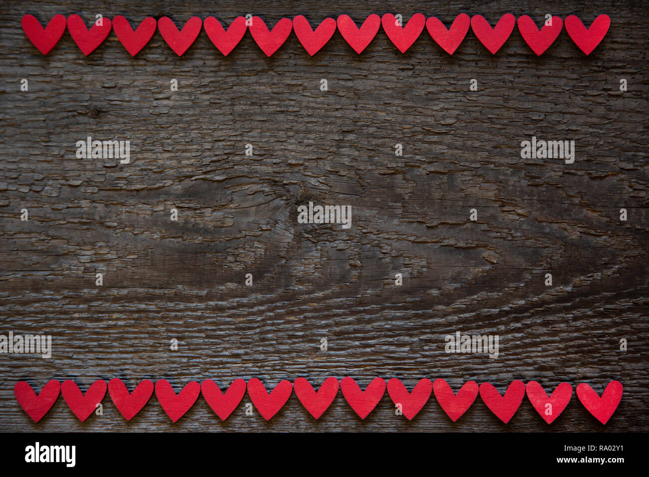 I cuori rossi sono posizionati orizzontalmente sui bordi superiore ed inferiore del vecchio legno marrone legno secco board. Il giorno di San Valentino Card Foto Stock