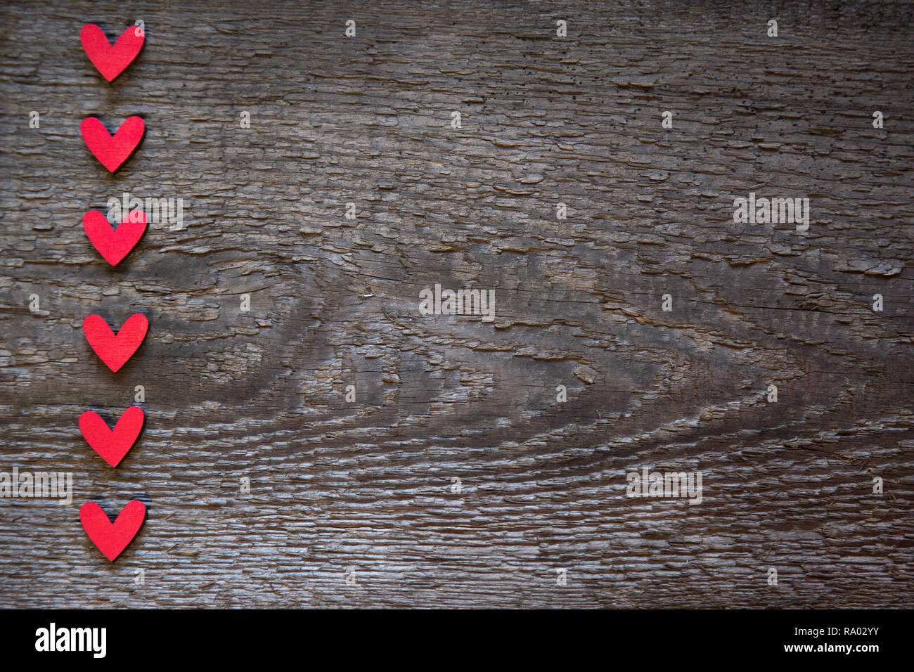 I cuori rossi sono disposte verticalmente sulla sinistra su un vecchio legno marrone scheda secco. Il giorno di San Valentino Card Foto Stock