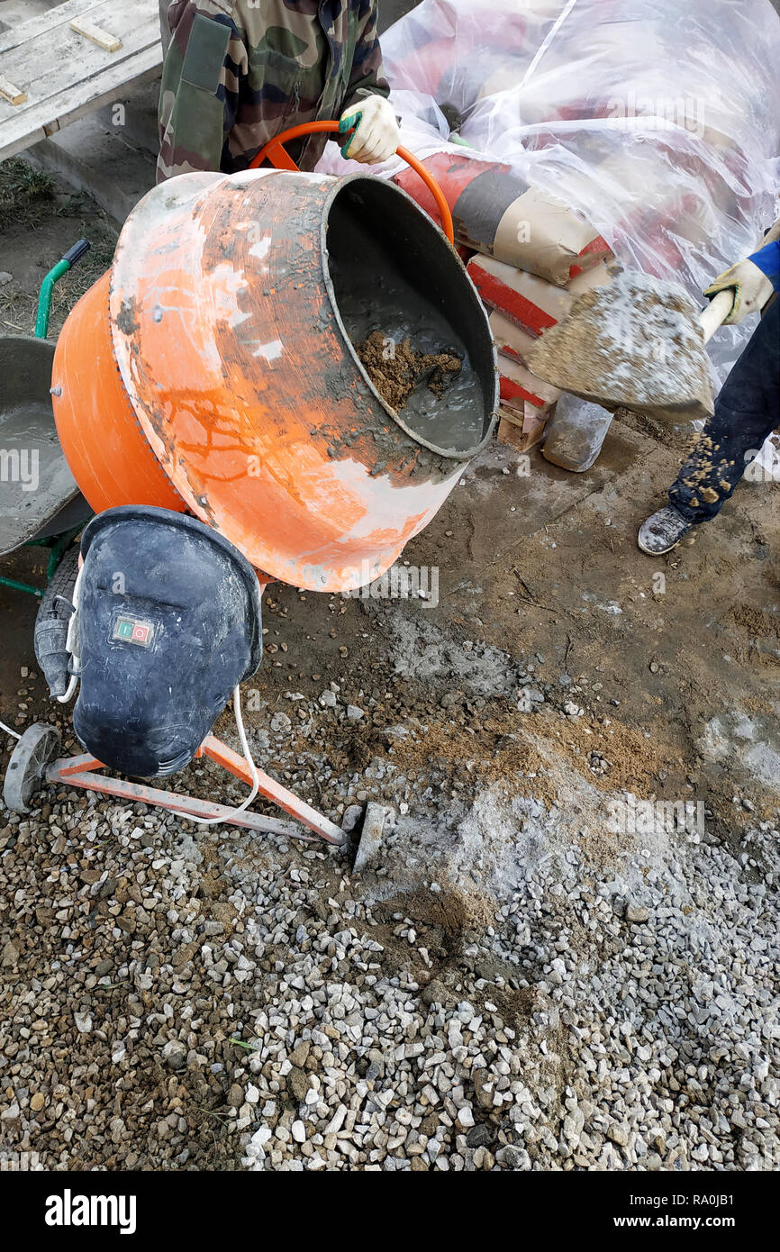 Lavoratore ausiliario si sviluppa una malta cementizia in un mescolatore concreto alla costruzione di una casa di campagna 2018 Foto Stock