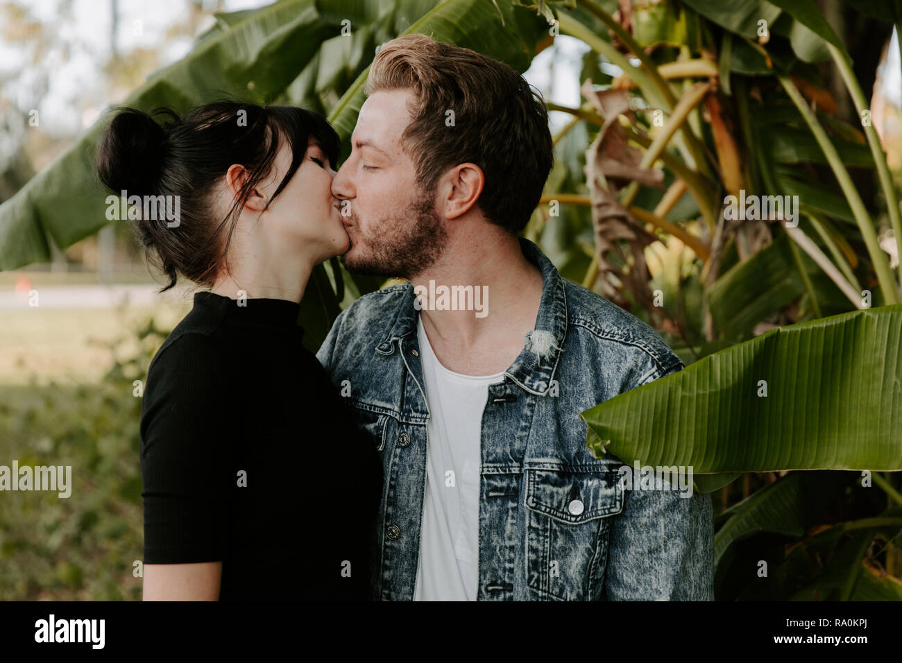 Ritratto di due simpatici caucasico moderno bella giovane adulto ragazzo fidanzato Lady ragazza giovane abbracciando e baciando in amore, Natura con piante verdi Foto Stock