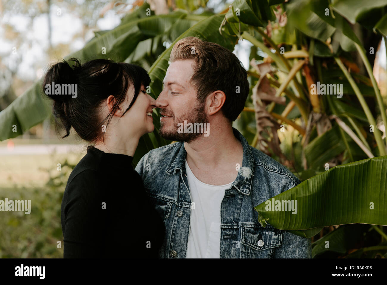 Ritratto di due simpatici caucasico moderno bella giovane adulto ragazzo fidanzato Lady ragazza giovane abbracciando e baciando in amore, Natura con piante verdi Foto Stock