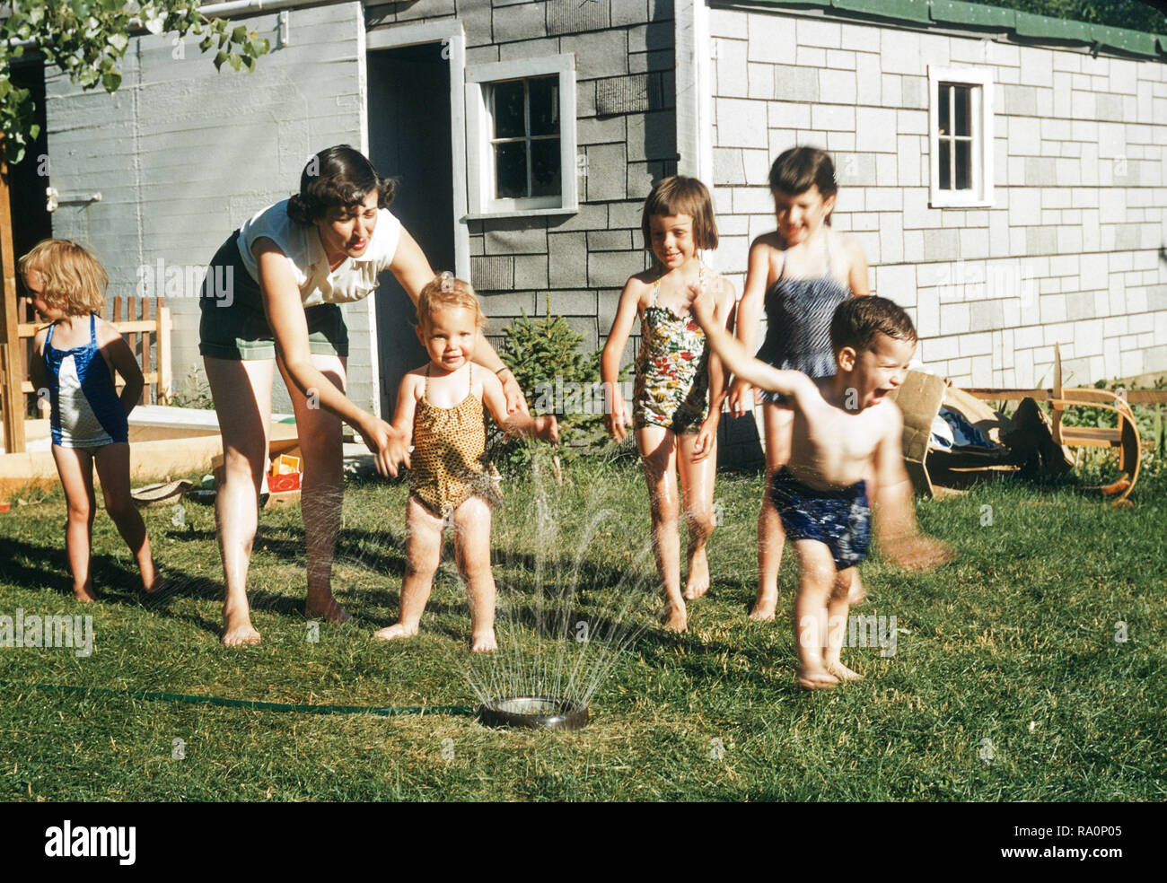 Anni Cinquanta la madre a guardare i bambini giocare in sprinkler, STATI  UNITI D'AMERICA Foto stock - Alamy