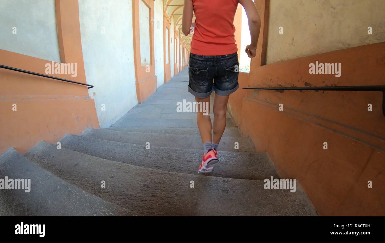Gambe di donna in esecuzione sotto San Luca Archway, Portico più lungo del mondo che porta a Bologna centro, nord Italia. Foto Stock