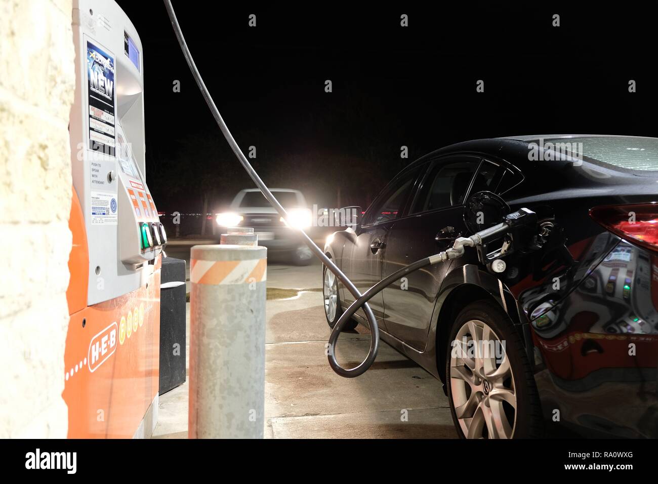 Rifornimento di carburante fino ad una stazione di gas durante la notte; veicolo in avvicinamento con i fari accesi; la gassificazione; riempiendo l'auto. Foto Stock