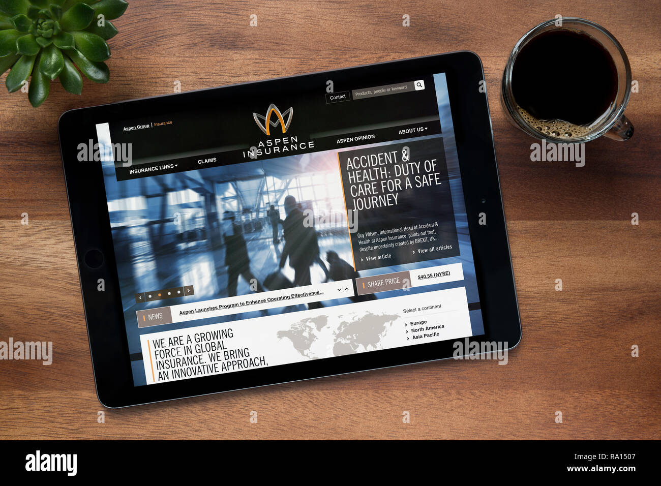 Il sito web di Aspen assicurazione è visto su un tablet iPad, su di un tavolo di legno lungo con un caffè espresso e una pianta di casa (solo uso editoriale). Foto Stock