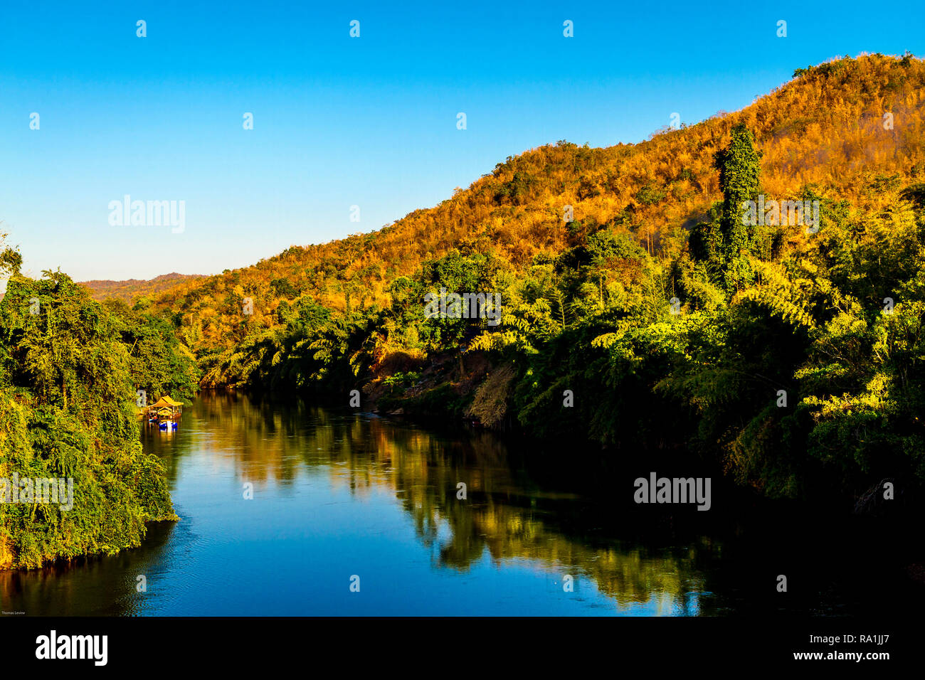 Guardando verso il centro del fiume con la giungla su entrambi i lati e un profondo cielo blu. Una piccola barca casa è giù il fiume. Foto Stock