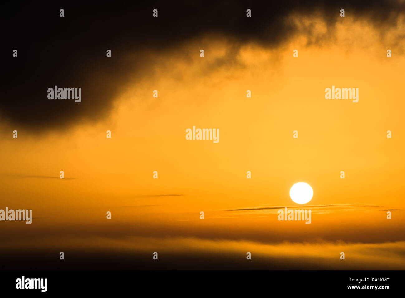 Il sole splende in arancione come una palla di fuoco tra due strati di cloud Foto Stock