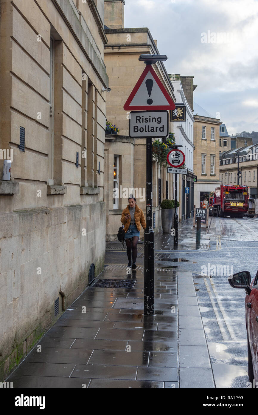 Pedone cammina verso una forma triangolare segno di attenzione avverte di un aumento bollard in strada nella parte inferiore delle pareti di Borough nella città di Bath Foto Stock