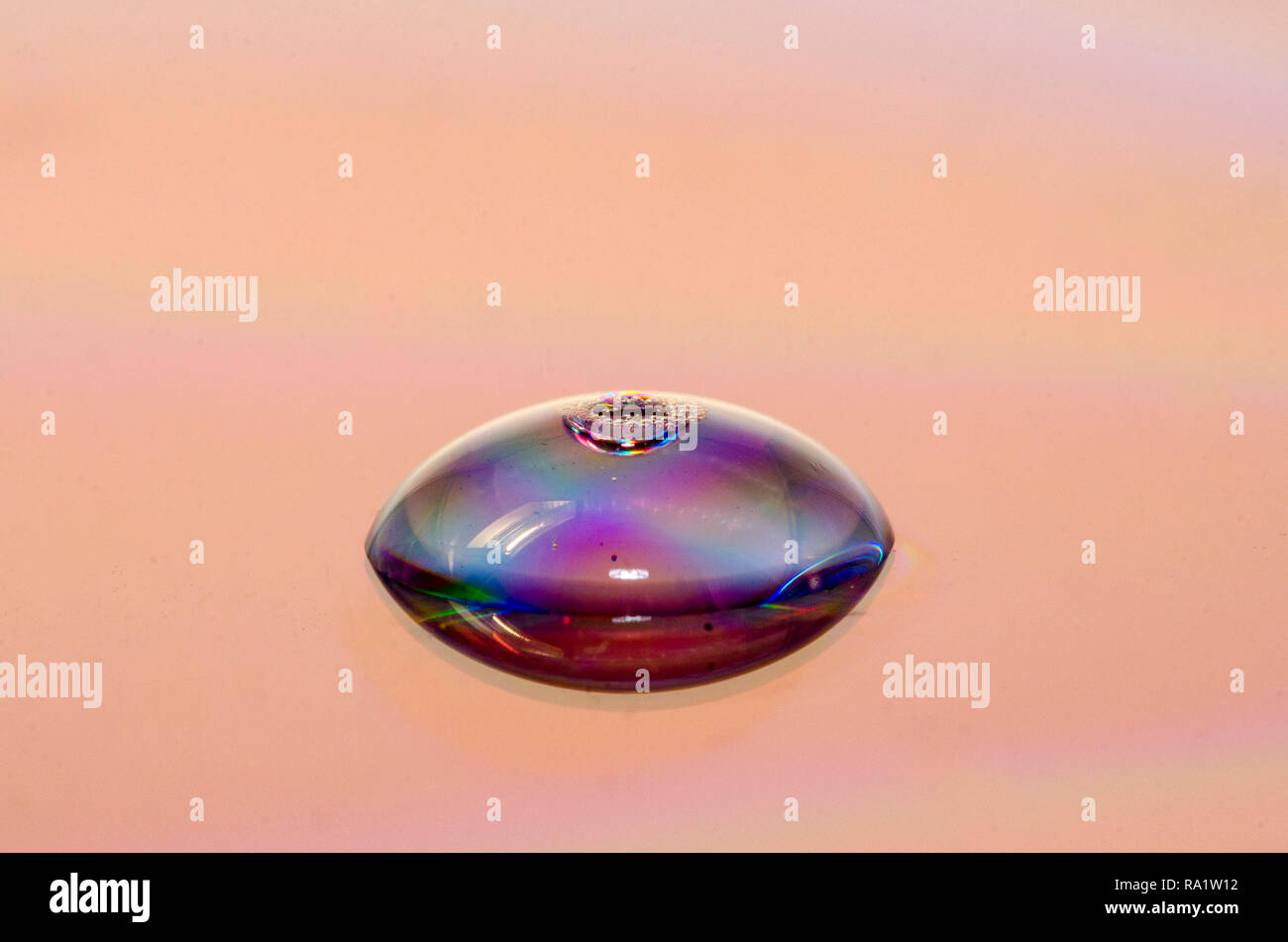 La rifrazione della luce su una goccia di acqua al di sopra di una superficie colorata Macro di una goccia di acqua al di sopra di una superficie a specchio Foto Stock