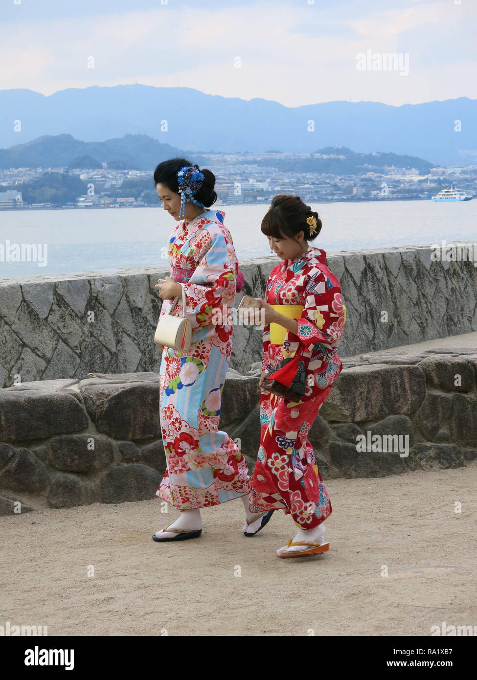 Due giovani donne nella tradizionale kimono giapponese a piedi lungo il mare  sull'isola di Miyajima, Giappone; entrambi i sacchetti di contenimento e  telefoni cellulari Foto stock - Alamy