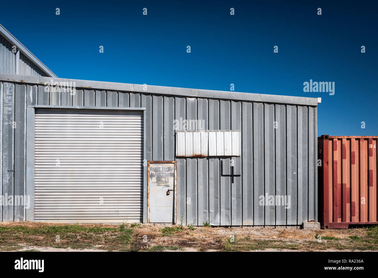 Argento metallico ondulato edificio con il rullo porta e rosso contenitore di cartone ondulato a lato Foto Stock