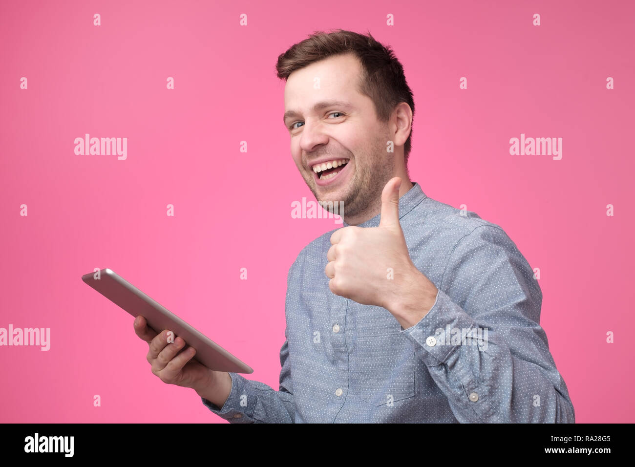 Uomo con tablet sollevamento pollice in alto e sorridente largamente, dando feedback positivo Foto Stock