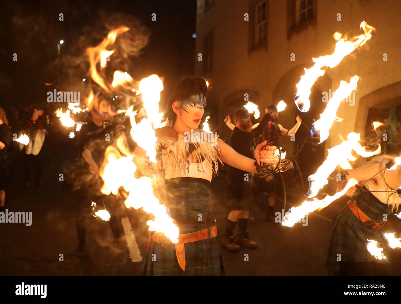 I membri della pionieristica compagnia teatrale Celtic Fire della Scozia, PyroCeltica, in abbigliamento completo Highland Warrior con claymores fiammanti e personale antincendio che conduce una sfilata di fiaccolate lungo il Royal Mile durante le celebrazioni dell'Hogmanay di Edimburgo. Foto Stock