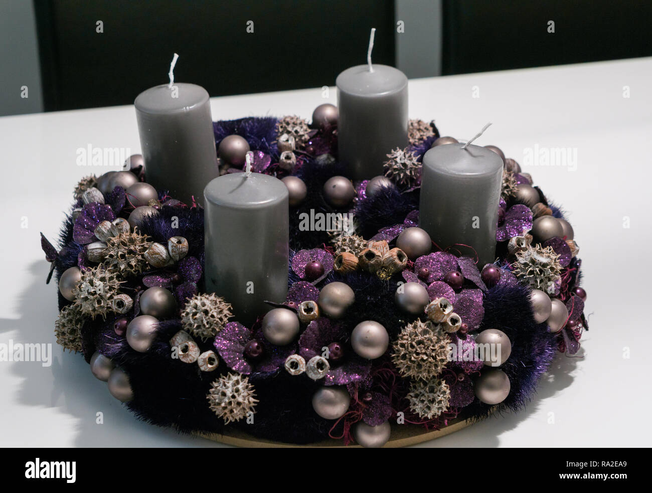 Viola corona di Avvento con baubles e quattro candele grigio su un tavolo bianco Foto Stock
