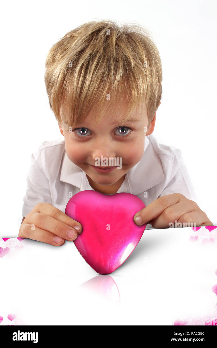 Bambino ragazzo tenendo un a forma di cuore ad oggetto metallico per San Valentino, Festa della Mamma, con un biglietto di auguri dire ti amo Foto Stock