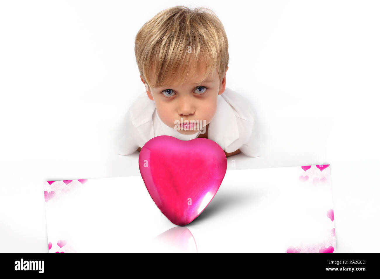 Bambino ragazzo tenendo un a forma di cuore ad oggetto metallico per San Valentino, Festa della Mamma, con un biglietto di auguri dire ti amo Foto Stock