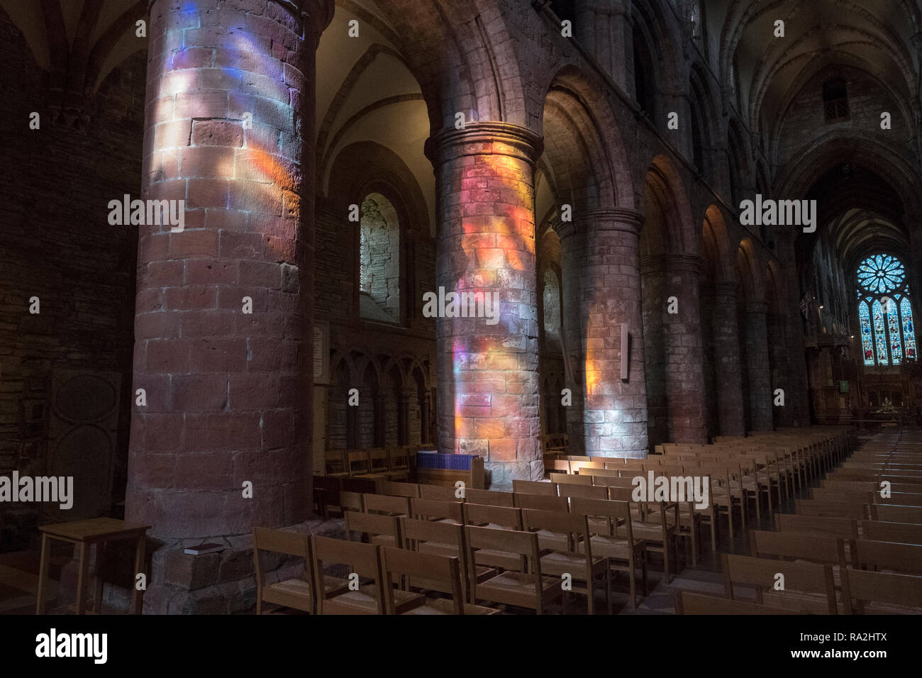 Archi interni di San Magnus Cathedral a Kirkwall sono illuminate da un arcobaleno di luce proveniente attraverso le vetrate della facciata occidentale Foto Stock