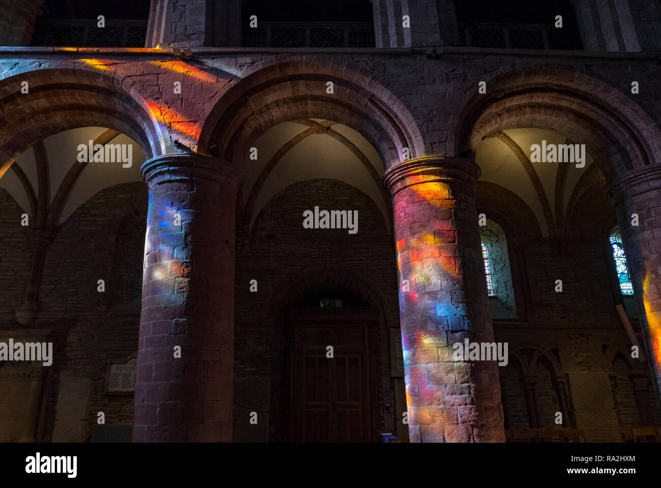 Archi interni di San Magnus Cathedral a Kirkwall sono illuminate da un arcobaleno di luce proveniente attraverso le vetrate della facciata occidentale Foto Stock