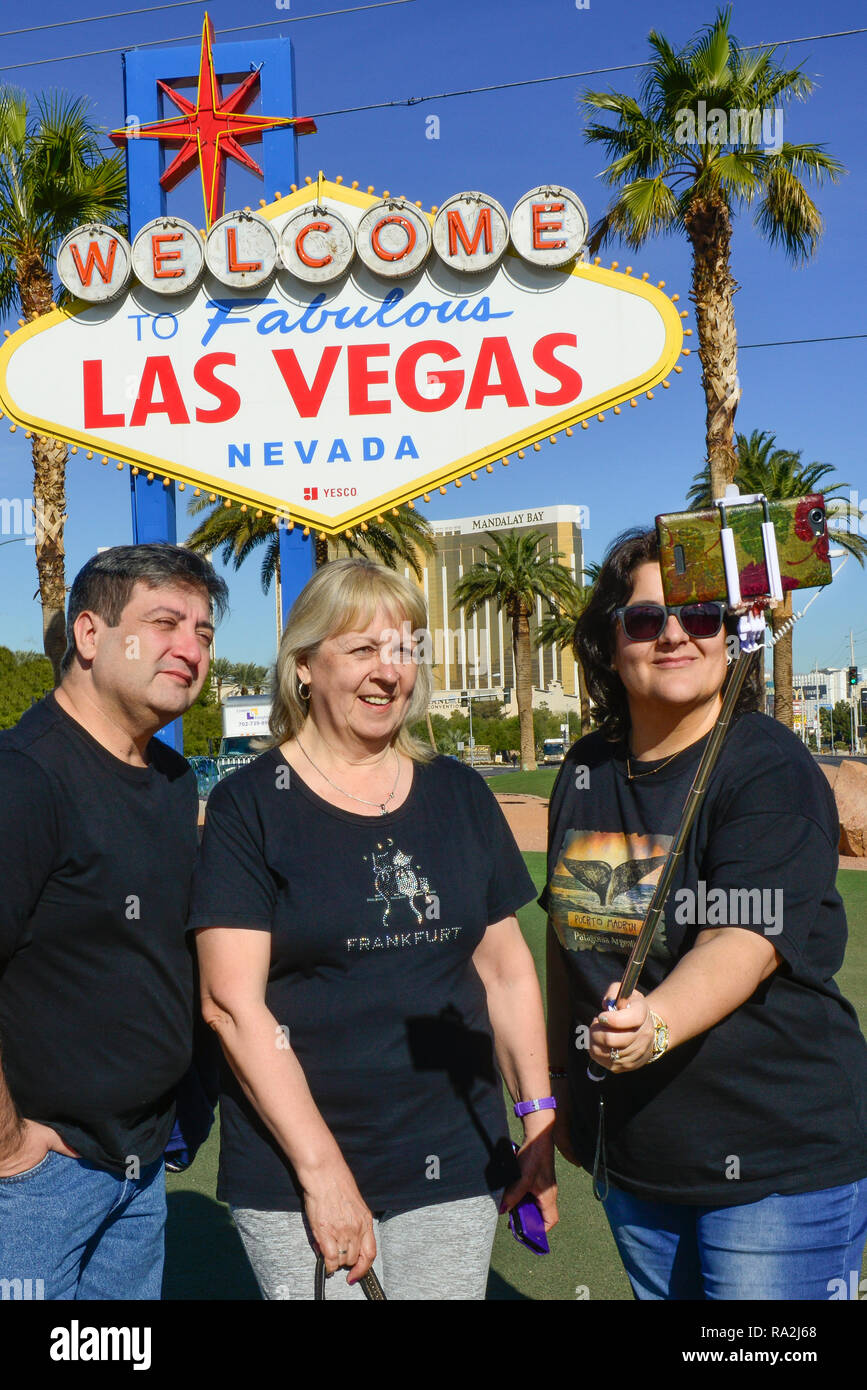 Uomo con due donne a posare per foto utilizzando una bacchetta selfie davanti al famoso, vintage, 'Benvenuti al favoloso Las Vegas, Nevada' segno in ingresso a striscia Foto Stock