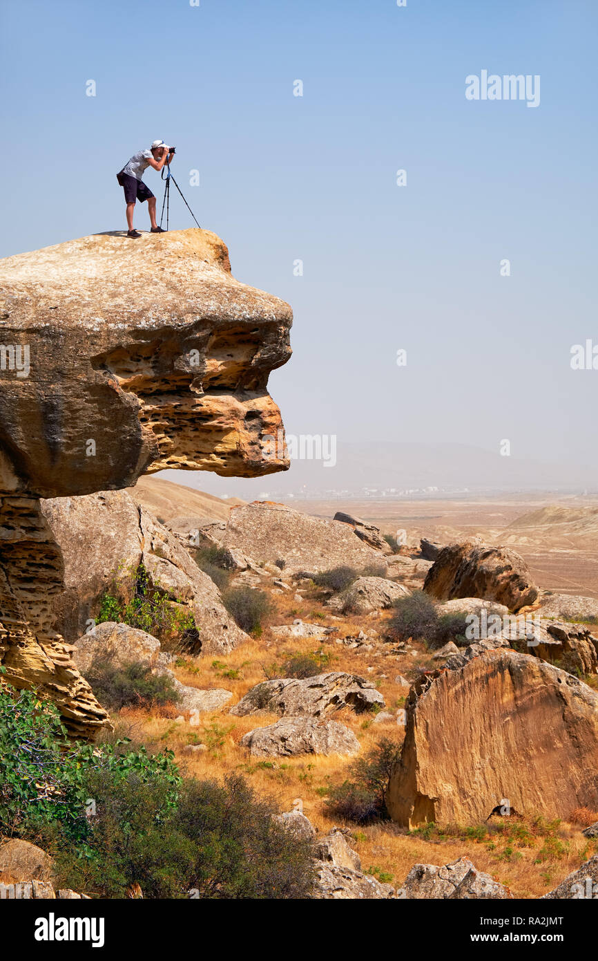 Fotografo con treppiede a sbalzo al disopra del piano roccia. Gobustan, Azerbaigian. Foto Stock
