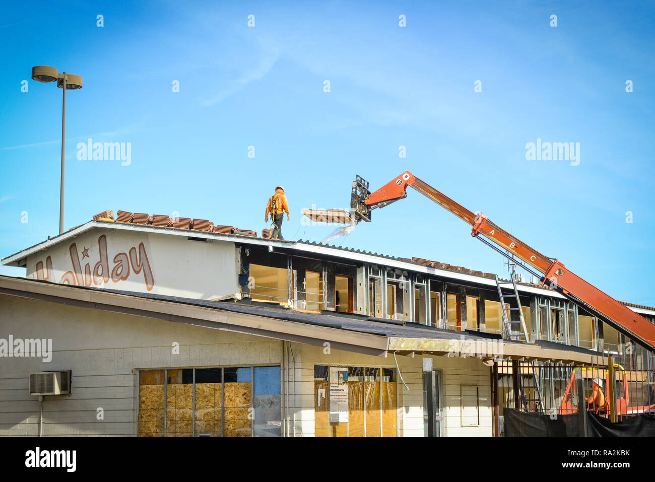 Un lavoratore edile che indossa un elmetto passeggiate sul tetto lungo con gru deliverying pallet di piastrelle in argilla tetto per rimodellare su un vecchio motel in Las Vegas Foto Stock
