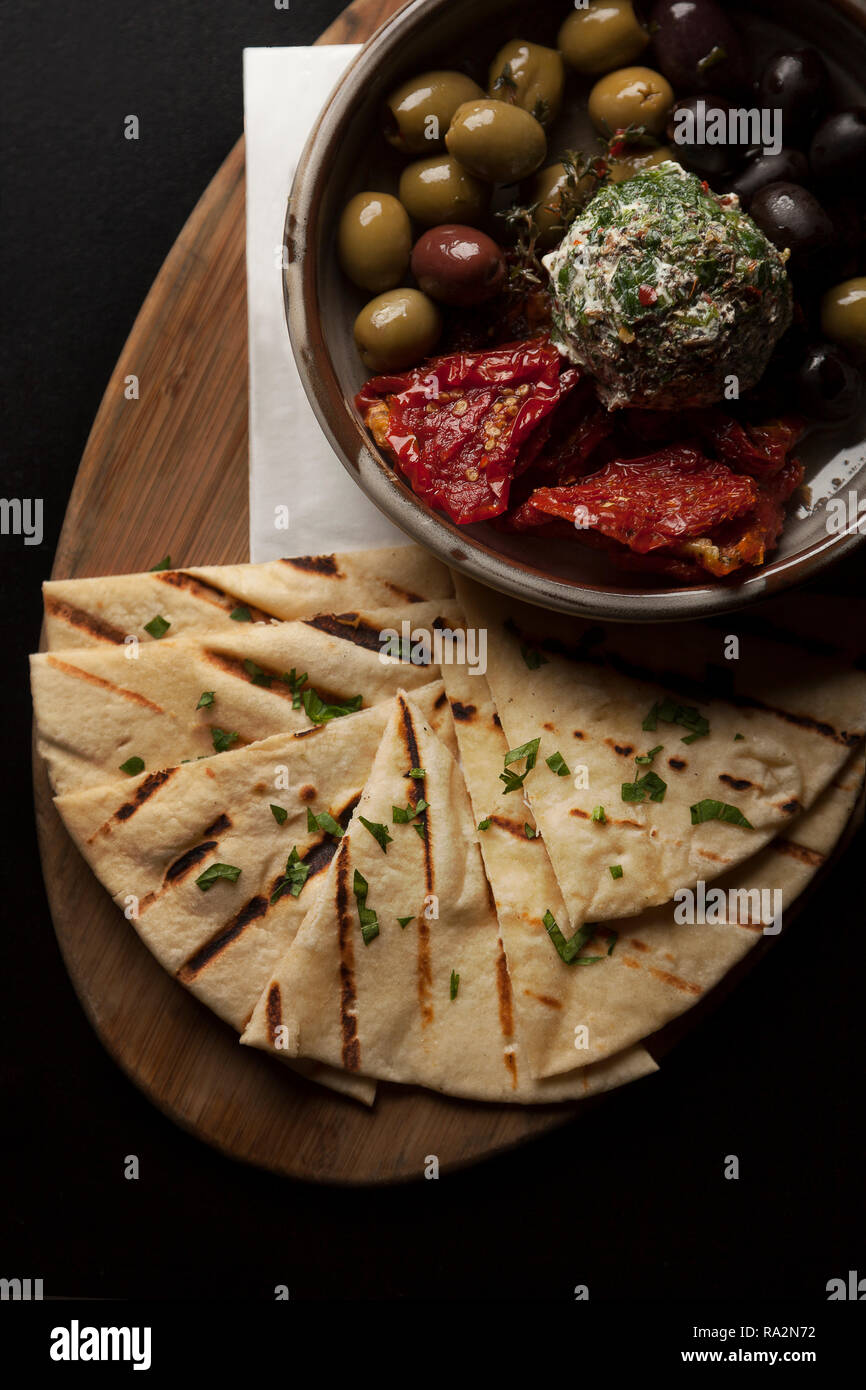 Pane Pita servita con pomodori secchi e olive & tzatziki dip su una tavola di legno che serve board. Foto Stock