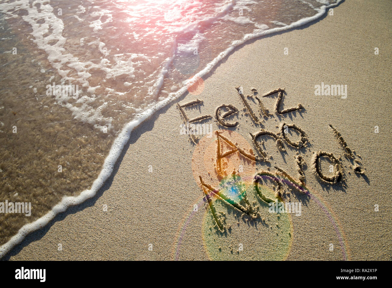Il portoghese Feliz Ano Novo (Felice Anno Nuovo) messaggio scritto a mano in caratteri a trama sulla sabbia liscia con una nuova onda su una spiaggia brasiliana Foto Stock