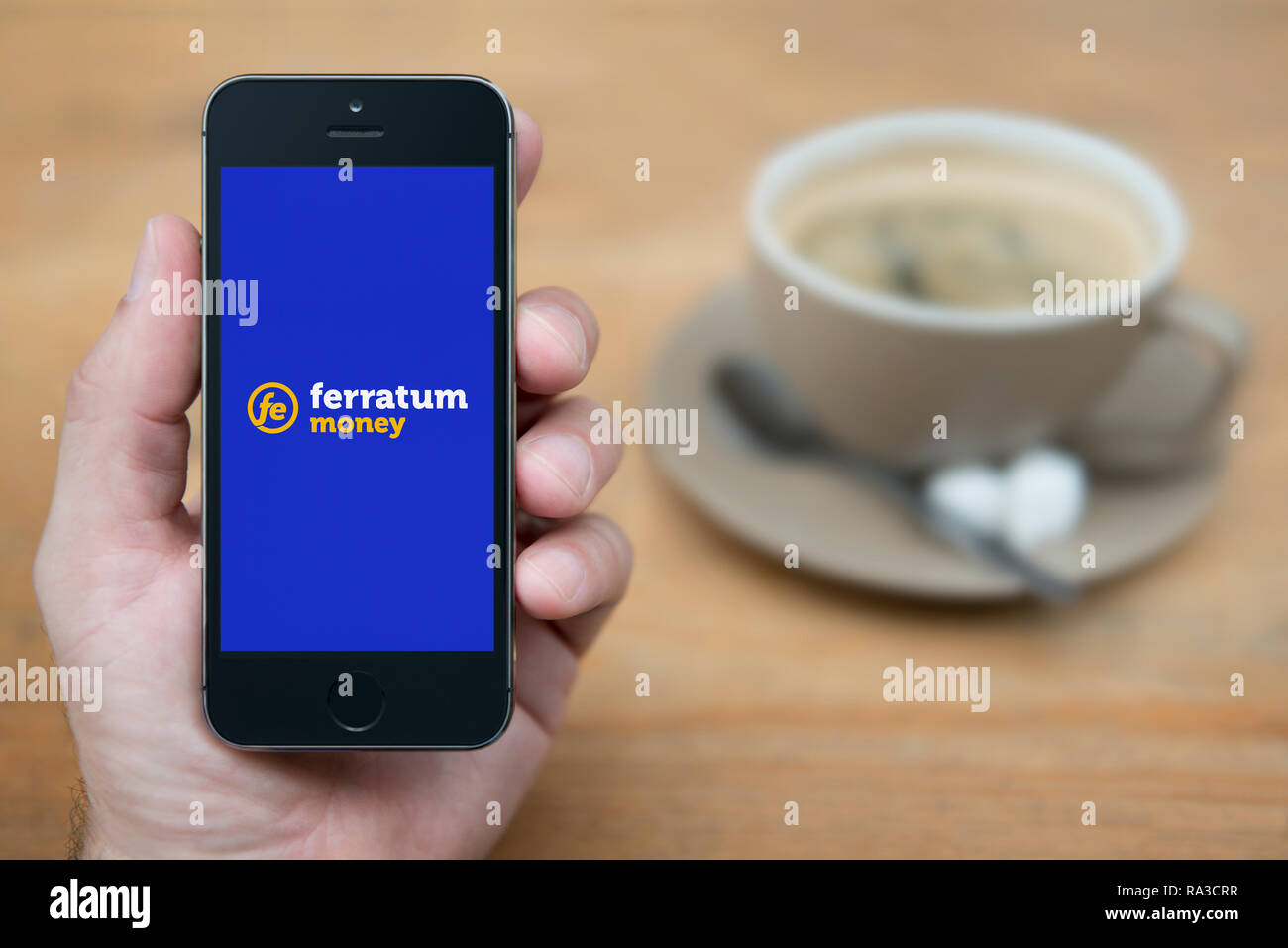 Un uomo guarda al suo iPhone che visualizza il logo Ferratum (solo uso editoriale). Foto Stock