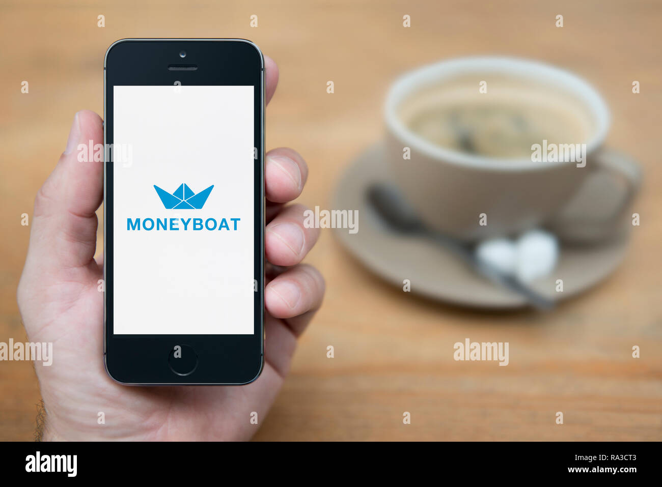 Un uomo guarda al suo iPhone che visualizza il logo Moneyboat (solo uso editoriale). Foto Stock