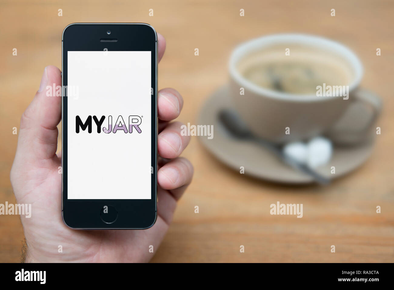 Un uomo guarda al suo iPhone che visualizza il logo MyJar (solo uso editoriale). Foto Stock
