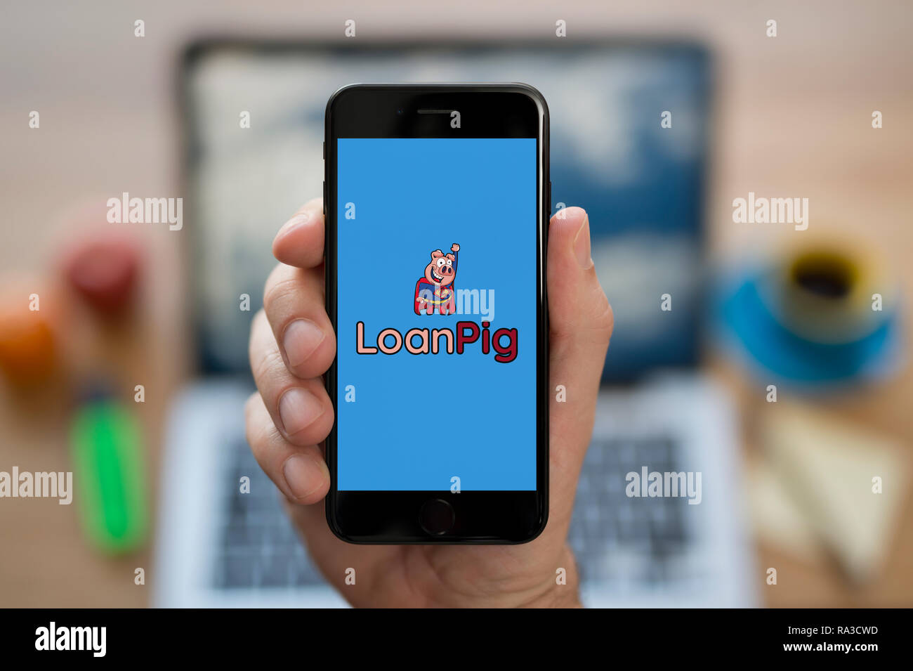 Un uomo guarda al suo iPhone che visualizza il logo LoanPig (solo uso editoriale). Foto Stock