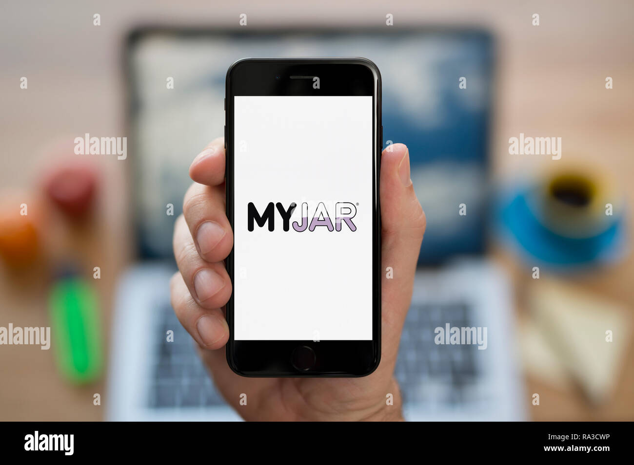 Un uomo guarda al suo iPhone che visualizza il logo MyJar (solo uso editoriale). Foto Stock