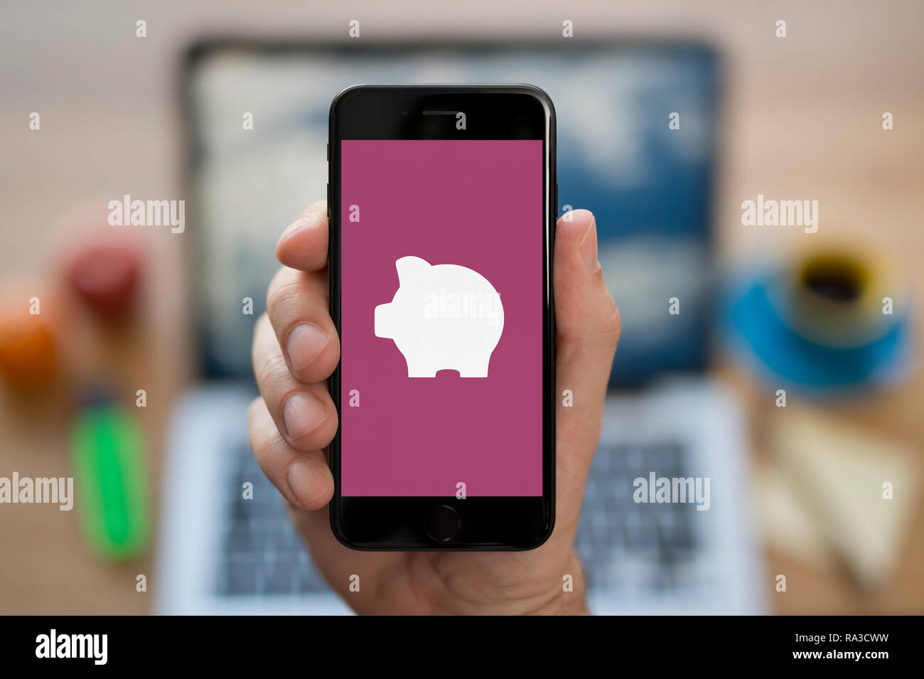 Un uomo guarda al suo iPhone che visualizza il logo Piggybank (solo uso editoriale). Foto Stock