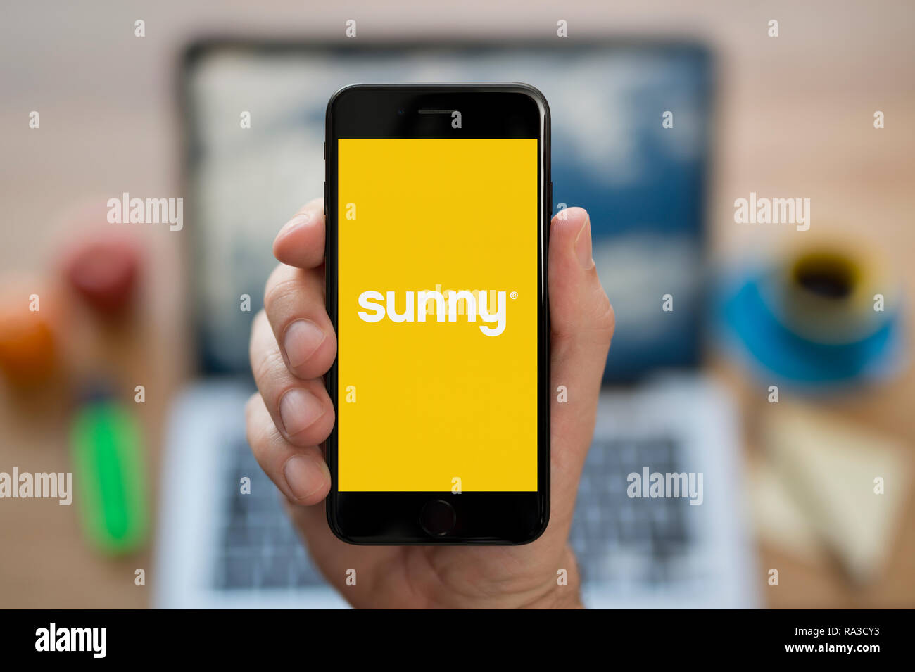Un uomo guarda al suo iPhone che visualizza il logo di sole (solo uso editoriale). Foto Stock