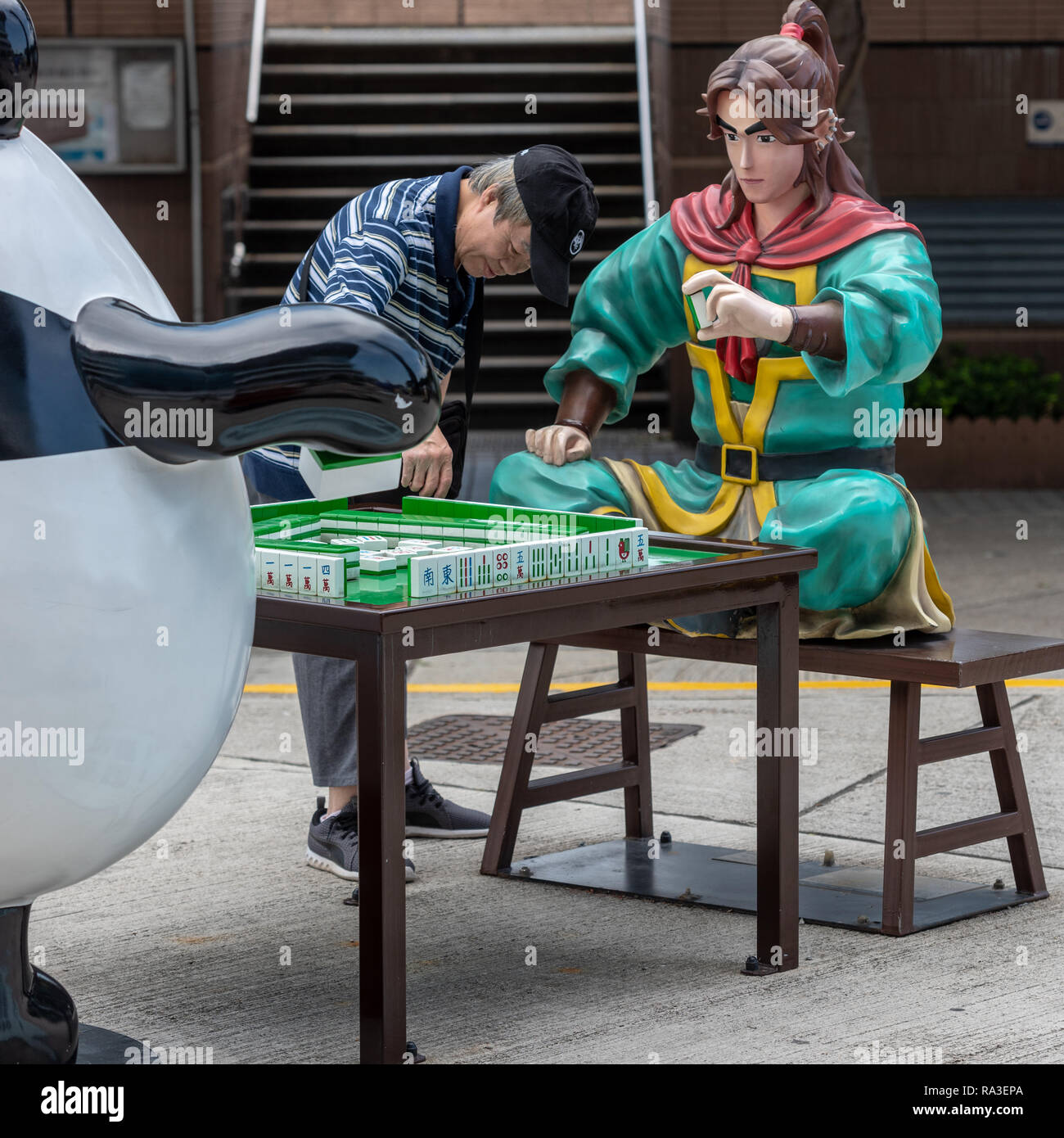 Un turista esamina Liao Yuan Huo's mahjong piastrelle come egli contesta un gioco con su On e Guy Guy a Ani-Com Park di Hong Kong Foto Stock